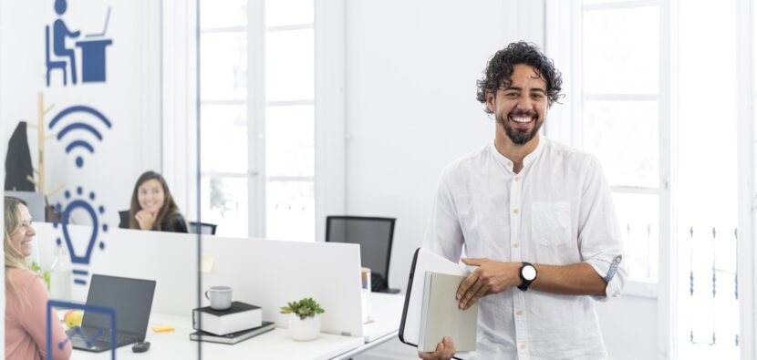 Portrait of a businessman holding documents and smiling in a modern office with his coworkers working